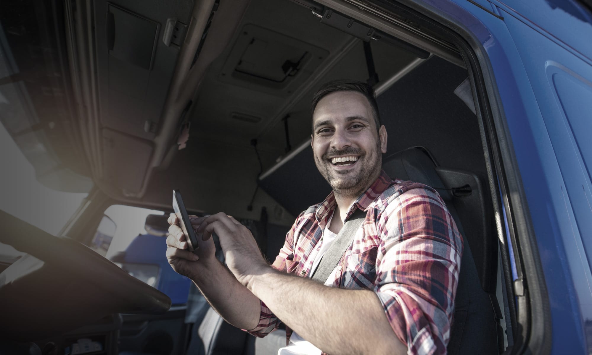 Lkw-Fahrer lächelt und bedient ein Smartphone in der Fahrerkabine.